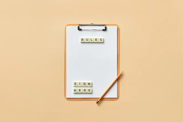 Flat lay of clipboard with letter tiles spelling 'rules' and 'sign here', accompanied by pencil on beige background. Athlete lookalikes submission rules: what contest desks check first