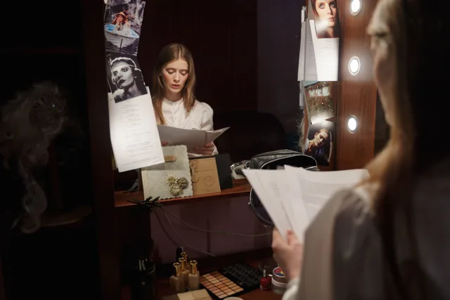An actress reviews her script in front of a mirror backstage with thoughtful expression. Orlando theme-park lookalike hiring cycles and seasonal pay