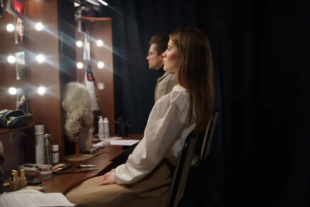 Two actors in a theater dressing room preparing for a performance, sitting and reviewing scripts. Professional lookalikes pairs: consent from only one side of the frame