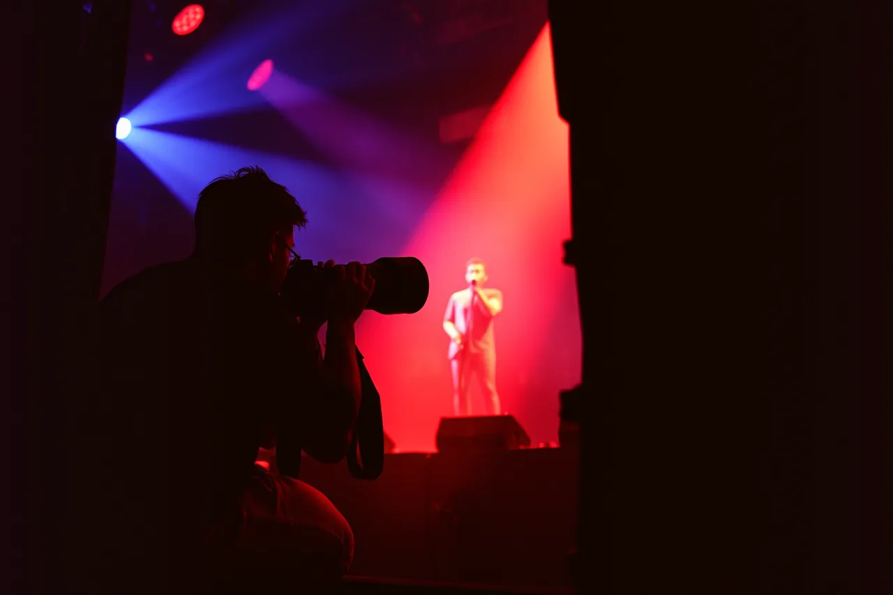Pit photographer with long lens shooting a performer under colored stage light (Musician lookalikes comparison: the record, kept honest)